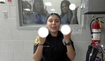 Una mujer con uniforme saca la lengua ante la cámara mientras tres personas hacen gestos detrás de un ventanal de vidrio