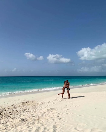 La pareja, abrazada y con el cabello mojado, posa frente a cámara con el mar y la vegetación densa de fondo