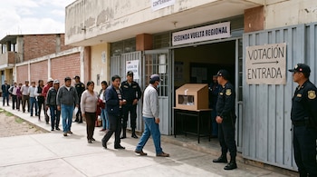 Fila de personas frente a la entrada de un centro de votación con carteles informativos y custodia policial en Perú.