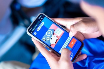 Primer plano de manos sosteniendo un smartphone mostrando una pantalla con gráficos sobre ahorro de emergencia, incluyendo una alcancía y símbolos de dinero