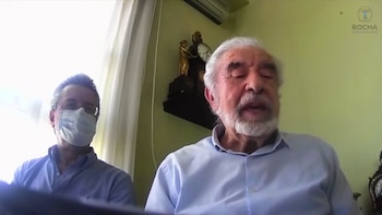 Rafael del Castillo, un hombre mayor con barba blanca, hablando. Detrás, un hombre con mascarilla y gafas, y un reloj ornamental en la pared
