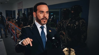 Abelardo de la Espriella trajeado señala hacia abajo al hablar, con hombres uniformados y reclusos en trajes naranjas al fondo.