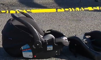 Una silla de seguridad negra para bebé reposa sobre el asfalto detrás de una cinta de precaución policial amarilla