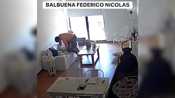Video de seguridad muestra a un hombre sin camisa agachado sobre una persona en un sofá claro, en una sala con piso de madera y ventana