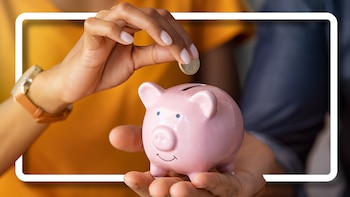 Primer plano de unas manos, una de ellas depositando una moneda de euro en una alcancía rosa en forma de cerdito. La otra mano sostiene la alcancía