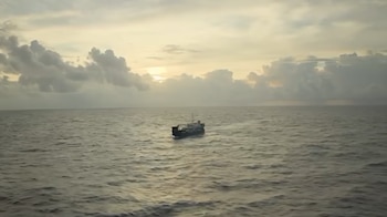 Un barco navega en mar abierto bajo un cielo nublado durante el atardecer
