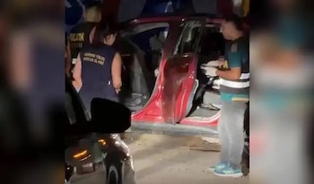 Un policía y personal del Ministerio Público revisan el interior de un automóvil rojo con las puertas abiertas durante la noche