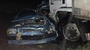 Automóvil azul claro con frente destrozado tras colisionar con un camión blanco. Se observan daños en la carrocería y el motor expuesto