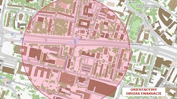 Mapa urbano que representa calles, edificios y áreas verdes. Un círculo rojo delimita una zona central. Un cartel indica 'Orientacyjny Obszar Ewakuacji'