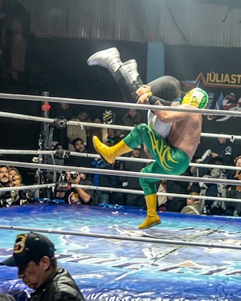 Dos luchadores sobre un cuadrilátero de lucha libre rodeado por cuerdas y espectadores en el fondo