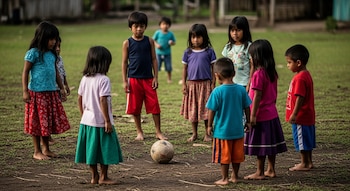 Ocho niños descalzos, con ropa de colores, de pie alrededor de un balón de fútbol viejo en un campo de tierra y césped ralo.
