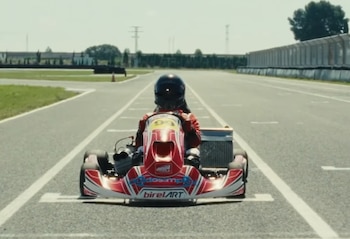 Un kart rojo y blanco con el número noventa y nueve y un piloto con casco negro sobre una pista de asfalto