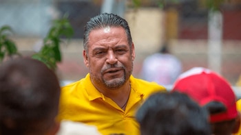 Primer plano de Luis Revilla, un hombre de mediana edad con cabello oscuro peinado hacia atrás y barba, vistiendo una camisa polo amarilla, rodeado de personas