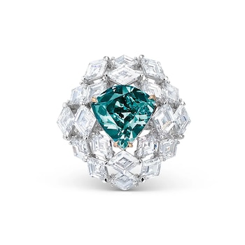 Anillo de compromiso de cerca con un diamante central verde azulado de talla cojín, rodeado por múltiples diamantes blancos sobre un fondo blanco