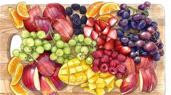 Tabla de madera con manzanas en rodajas, uvas verdes, uvas moradas, naranjas cortadas, moras, fresas, frambuesas y mango en cubos.