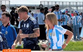 Ian Lucas y Renata Mónaco, con camisetas de Argentina, caminan entre una multitud de aficionados. Él tiene cabello rubio y ella cabello largo y rubio
