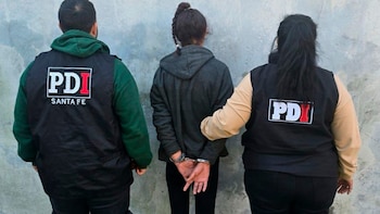 Una persona esposada, vista de espaldas, flanqueada por dos agentes con chalecos negros de la PDI Santa Fe, frente a una pared