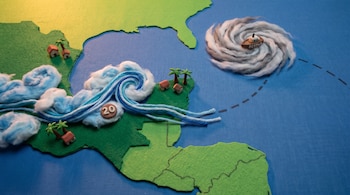 Mapa de fieltro azul y verde. Nubes, hilos y el número 20 sobre la tierra. Espiral de lana gris con barco "Bertha" en el mar, mostrando una ruta punteada.