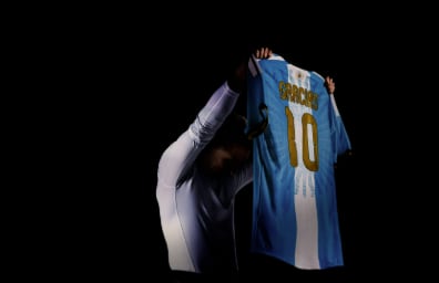 El futbolista Lionel Messi sostiene la camiseta de la selección argentina con el número diez y la palabra Gracias estampada en dorado.