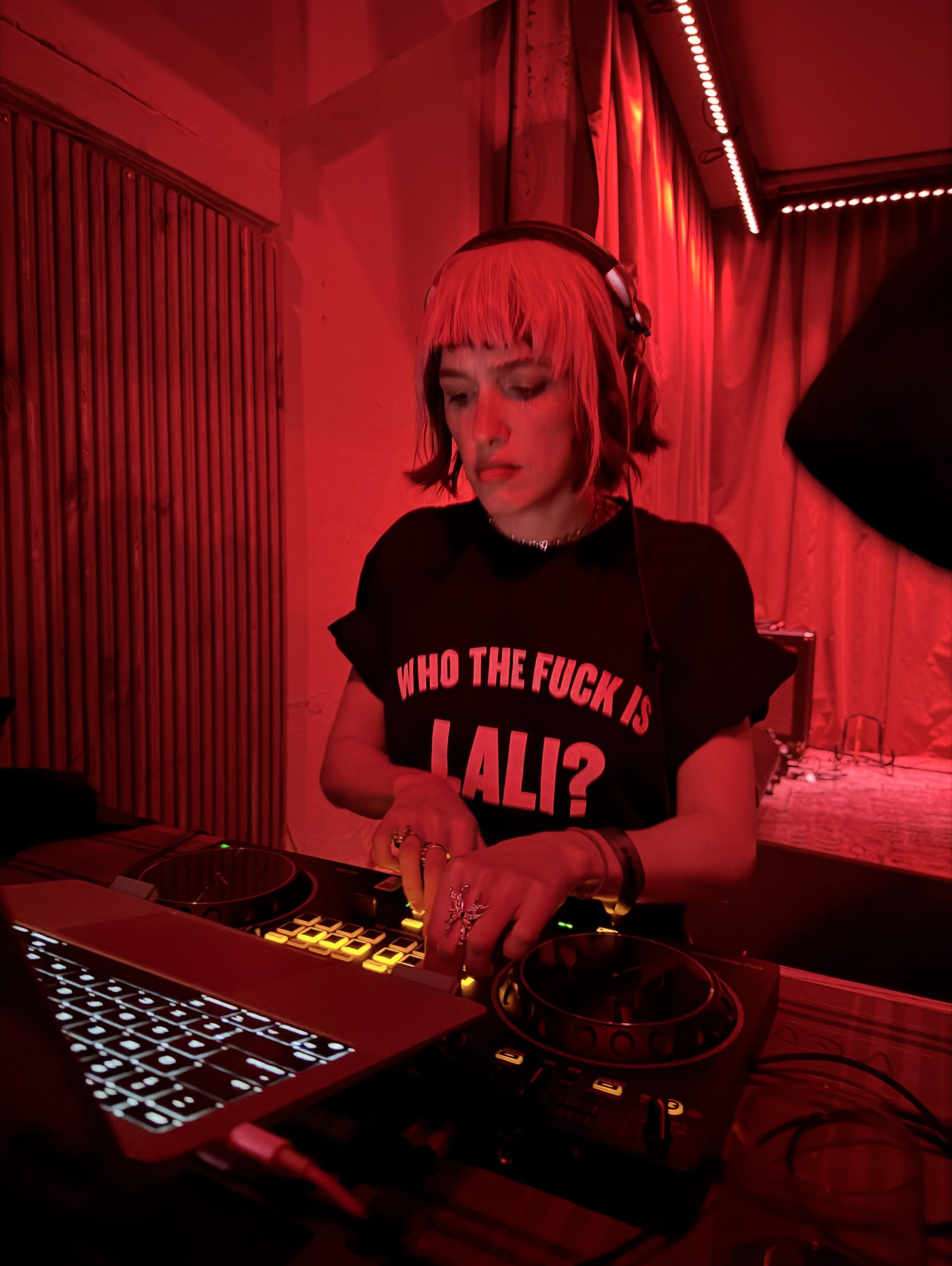La artista Lali Espósito opera una consola de sonido e instrumentos digitales en un ambiente iluminado por luces rojas.