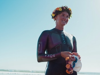 Una mujer con traje de neopreno oscuro, corona de flores en la cabeza y un gorro de natación en las manos al aire libre