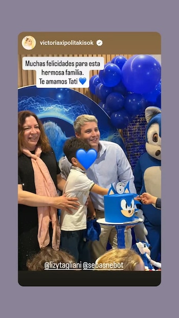 Lizy Tagliani junto a un hombre y un niño ante una torta azul con el número seis, globos azules y un personaje de traje azul