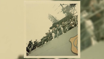 Fotografía en color de miembros de la tripulación naval en el puente de un barco, mirando hacia arriba. Una gran antena de radar se ve en el fondo