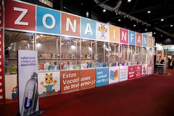 Puesto de la "Zona Infantil" en una feria de libros con paneles de colores, estantes llenos de libros y una señal de "Smartwater" al frente