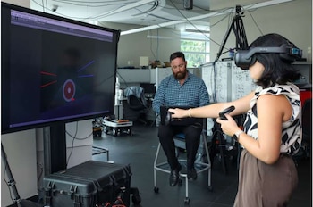 Un hombre con barba usa una computadora portátil frente a una pantalla grande con gráficos digitales tridimensionales