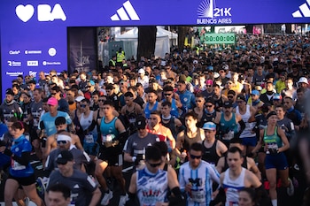 Multitud de corredores con ropa deportiva avanzan bajo una estructura violeta con patrocinios y un cronómetro digital