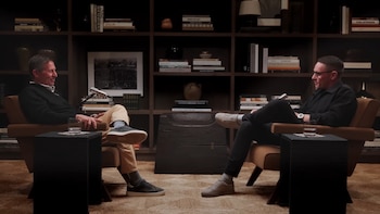 Dos hombres, uno es Dr. Paul Mischel, sentados en sillones de cuero marrón, conversando en un estudio con una estantería grande de madera llena de libros
