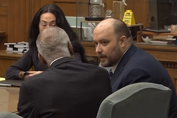Un hombre de barba con traje azul conversa con una persona de espaldas en la mesa de un tribunal junto a una mujer de cabello oscuro