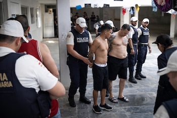 Agentes de Policía Penitenciaria esposan a dos hombres sin camisa en un patio de concreto. Varios policías con chalecos observan la escena.