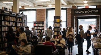 Interior de la Strand Bookstore en Nueva York, con numerosos clientes de diversas edades explorando estantes de libros, sentados y de pie.