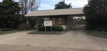 Entrada del barrio cerrado Campiña Elisa con garita de seguridad, un cartel con el nombre, portón cerrado, árboles y arbustos bajo un cielo nublado