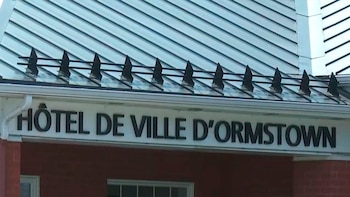 Primer plano del letrero "Hôtel de Ville d'Ormstown" en la fachada de un edificio de ladrillo rojo con techo metálico y adornos negros en el alero
