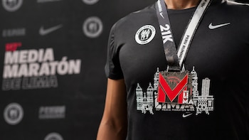 Persona con camiseta negra de deporte, medalla metálica con la letra M roja y detalles de edificios, cinta Peru Runners 21K, fondo oscuro con texto