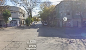 Vista de una calle con edificios a ambos lados, árboles, varios automóviles estacionados y dos marcadores de ubicación; en el asfalto se lee "Italia"