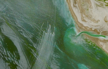 Vista satelital del Estrecho de Ormuz con agua verdeazulada y tierra beige. Se observan numerosas estelas y objetos blancos ascendiendo del agua