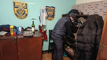 Hombre con gorra y chaleco oscuro organizando un estante. Al fondo, paredes azules con banderas de Boca Juniors y una camiseta de Argentina colgada.