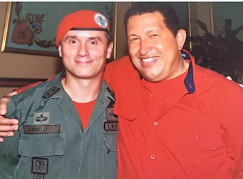 Fotografía de dos hombres sonriendo; uno con boina roja y uniforme militar verde oliva, el otro con camisa roja de cuello azul marino