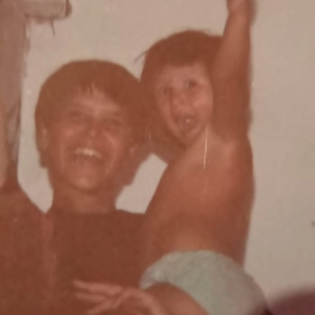 Imagen retro de dos niñas sonrientes, una con camiseta oscura sosteniendo a la otra, que lleva un pañal y tiene los brazos levantados