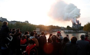 People watch from a bridge as smoke billows from Notre Dame Cathedral during a fire in Paris, France April 15, 2019. REUTERS/Benoit Tessier