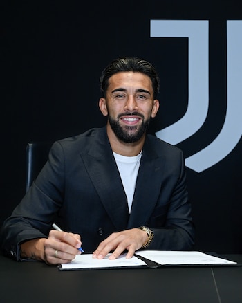 Nicolás González sonríe mientras firma un documento con un bolígrafo sobre un escritorio negro ante el logotipo de la Juventus