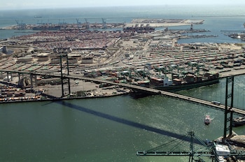Vista aérea de un puente colgante verde que cruza un canal de agua junto a un puerto repleto de contenedores y grúas
