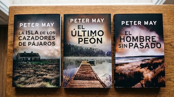 Tres libros de Peter May titulados La isla de los cazadores de pájaros, El último peón y El hombre sin pasado sobre una mesa de madera.