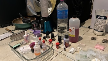 Frascos con líquidos, recipientes de vidrio, polvo blanco, una licuadora y una bolsa de lactosa dispuestos sobre un suelo de baldosas