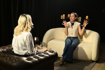 Pau Moguilevsky gesticula sentada en un sofá blanco frente a una entrevistadora en un estudio con fondo oscuro y velas