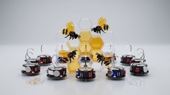 Un grupo de pequeños robots móviles, una maqueta de panal hexagonal con abejas de acrílico amarillo y negro, elementos hexagonales sueltos