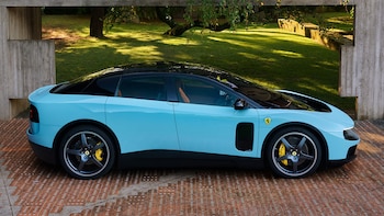 Vista lateral del Ferrari Luce, un coche eléctrico azul claro y negro, con diseño de berlina, estacionado sobre pavimento de ladrillo frente a césped